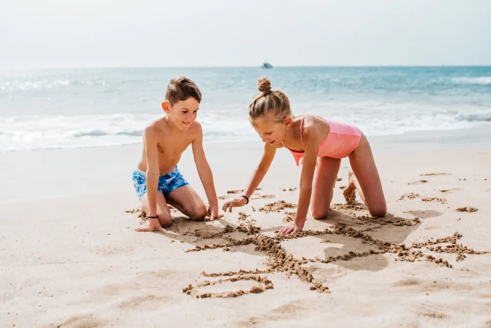 Two kids drawing in the sand at the beach, the photo